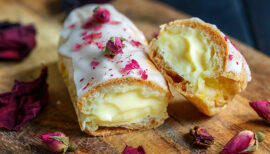 Eclair à la vanille recouvert de pétales de rose posé sur une table en bois