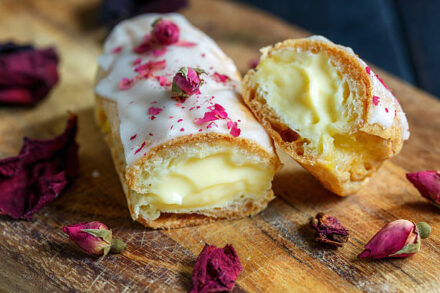 Eclair à la vanille recouvert de pétales de rose posé sur une table en bois