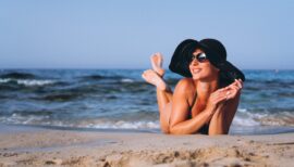 Femme avec un chapeau et des lunettes de soleil en train de bronzer sur le sable au bord de l'eau