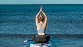 femme assise sur un paddle, bras au-dessus de la tête en posture de yoga