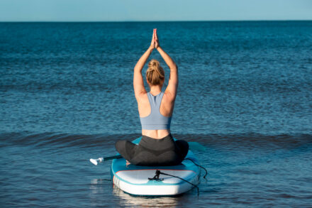 femme assise sur un paddle, bras au-dessus de la tête en posture de yoga