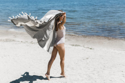 femme de profil, en bord de mer, serviette de plage au vent