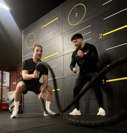 Séance de personal training à Genève dans une salle de sport haut de gamme, avec coach sportif et cliente en pleine exécution d’un exercice de renforcement musculaire.